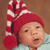 A pixelated close-up of a child wearing a red and white striped hat with a pom-pom, against a brown background.
