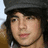 Pixelated close-up of a person with dark hair wearing a dark cap and brown garment, set against a light background.