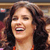 Static 50x50 pixel icon showing a close-up of a person with long dark curly hair wearing an orange top, smiling broadly with eyes closed and mouth open in laughter.