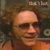 A static image shows a person with curly brown hair wearing glasses and an orange shirt, with orange text reading 'that's hot.' in the top-right corner.