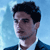 Pixelated portrait of a person with dark hair wearing a dark jacket over a light shirt against a light blue background.
