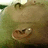 Pixelated close-up of a light brown animal face with dark eyes and nose, set against blurred green foliage background.