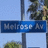 Blue street sign with white text reading 'Wells St' and 'Ave', mounted on a pole against a light blue sky background.