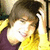A person with brown hair wearing a yellow sweater over a dark purple shirt, smiling and touching their head in multiple
