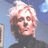 Pixelated portrait of a person with light-colored hair against blue background, wearing dark high-necked clothing.