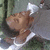 A person in a white tank top and gray jacket lies on grass with eyes closed, head tilted back, mouth slightly open.