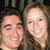 Two people with light skin tones pose closely together in a pixelated image, both smiling at the camera against a dark background.
