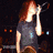 A person with long red hair sings into a microphone in three distinct poses across four , wearing different outfits against varied stage backgrounds