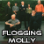 Pixelated static image of a band with multiple figures in dark clothing against a green background, featuring bold text at the bottom reading "FLOGGING MOLLY".