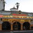 Pixelated static image of a building facade with arched windows, a central tower, and a cross atop the roof under a light sky.