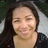 A static pixelated image shows a person with long dark hair, light skin tone, and closed eyes smiling while resting their head on one hand against a blurred background.