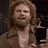 Pixelated image of a person with long brown hair wearing a light-colored top, holding a dark rectangular object against a checkered background.