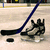 A static pixelated image shows a hockey stick, puck, and skates on an ice rink with blurred background elements.