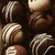 Pixelated brown and beige circular shapes with white highlights on a dark background, arranged in overlapping clusters.