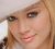 Pixelated close-up of a person's face with light brown hair, visible eyes, nose, and mouth against a blurred background.