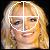 Pixelated static image of a person's face with blonde hair and a white cross overlay, rendered in warm tones on a dark background.