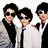 Three individuals in formal attire stand against a bright pink background with cyan text reading "LOVE the Jonas Brothers!!!" below.