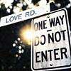 identical 'ONE WAY DO NOT ENTER' street signs with 'LOVE RD.' banners, each sign showing a bright light flare on the left side