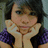 Pixelated image of a person with dark hair resting hands under chin, wearing purple and black top against blurred background.