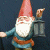 A garden gnome character with a red hat and white beard holding a lantern, next to green text reading "Original Icons .com" on a dark background.