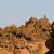 Pixelated landscape with brown and orange terrain under a light blue sky, featuring rocky formations and sparse green patches.