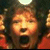 Pixelated close-up of a person with dark hair and orange-toned skin, mouth open in an expressive gesture against a blurred background.