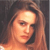 A pixelated close-up of a person with light brown hair against a dark background, showing the upper shoulders and face.