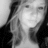 Pixelated grayscale image of a person with long hair, wearing dark clothing and holding hands near the face in a contemplative pose.