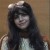 Pixelated static image of a person with long dark hair wearing light-colored clothing against a brown background.