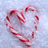 A heart-shaped arrangement of red-and-white striped candy canes on a light gray background, with text elements in bright pink and red sections.