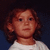 Pixelated portrait of a person with light brown curly hair wearing a white shirt against dark blue background.