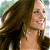 A static pixelated image of a person with long brown hair, light skin, and a neutral expression, wearing a dark top against a blurred background.