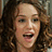 Pixelated close-up of a person with long dark curly hair, light skin tone, and open mouth showing teeth.
