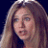 A pixelated close-up of a person with long light brown hair against a dark blue background, showing partial facial features and clothing details.