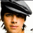 Pixelated close-up of a person wearing a dark flat cap with a light stripe, light brown skin, and a neutral expression against a white background.