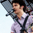 Pixelated image of a person with dark hair wearing a light purple shirt and dark straps, set against a light blue background.