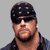 Static pixelated image of a person wearing a dark cap with white dots, sunglasses, and a black shirt against a gray background.