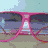Pink sunglasses with dark lenses rest on a light blue surface, showing reflections of the surrounding environment.
