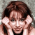 Pixelated static image of a person with brown hair holding hands near their face against a gray background.