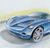 Pixelated blue car with black wheels on a light gray surface under a yellowish sky gradient.