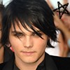 A close-up of a person with dark tousled hair, wearing a black jacket over a dark shirt, with a hand holding a black star-shaped object near the head.