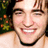 A pixelated close-up of a smiling person with light brown hair, visible teeth, and a black collar against a blurred green and orange background.