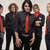 Group of people in dark uniforms with red ties, some with arms crossed, one person raising a hand, pixelated text overlays in white.