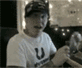 A person in a white U-shirt and dark cap performs sequential hand gestures against a blurred background with lights.