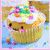 Pixelated cupcake with white frosting, colorful sprinkles, and a smiling face on a light blue background.