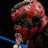 Pixelated static image of a figure with red-toned skin, dark hair, and blue clothing against black background.