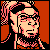 Pixelated static image of a character with light skin, dark hair tied in a ponytail, wearing glasses and a patterned top against an orange background.