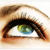 Pixelated close-up of a human eye with brown eyelashes, a dark brown iris, and a green-blue pupil against a light skin tone background.