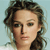 Pixelated close-up of a person with curly brown hair against a light blue background, showing facial features and hair texture in low-resolution.