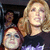A static image of a woman with blonde hair and a red-haired person in the foreground, both wearing dark tops with purple accents.